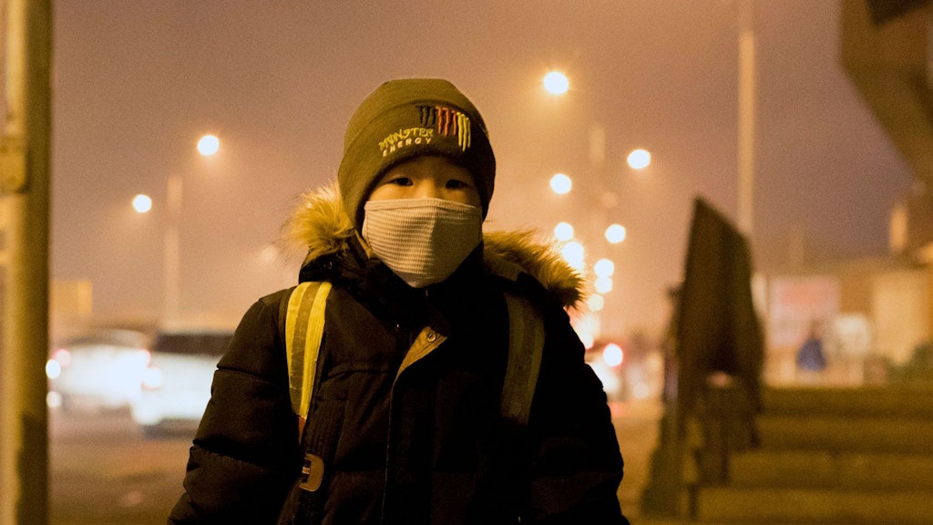 Ein Junge mit einem Schulrucksack und einer Gesichtsmaske wartet an einer Bushaltestelle in Ulaanbaatar.