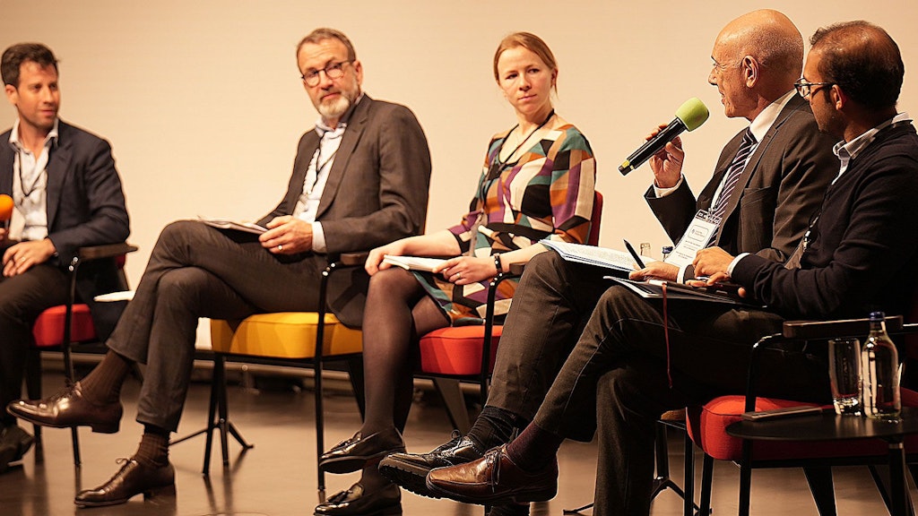  Vier Männer und eine Frau nehmen an einer Podiumsdiskussion teil.