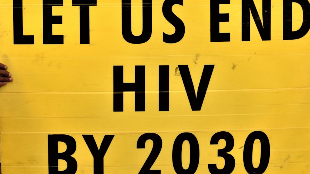 Ein junger Mann hält ein gelbes Plakat in die Luft auf welchem steht: «Wir wollen HIV bis 2030 besiegen.»