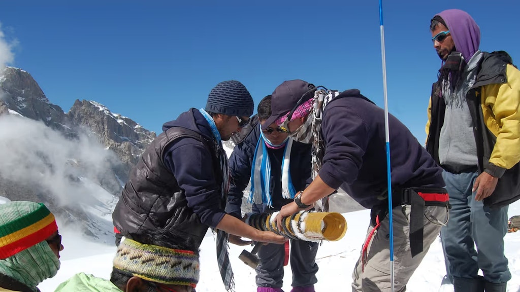 Sieben Männer führen auf einem Gletscher wissenschaftliche Messungen im Schnee durch. 