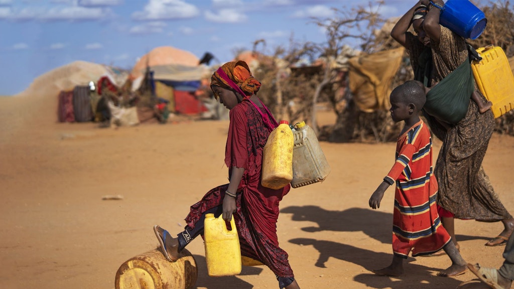 Des femmes et des enfants transportant des bidons d’eau dans un village formé de simples huttes en Somalie.