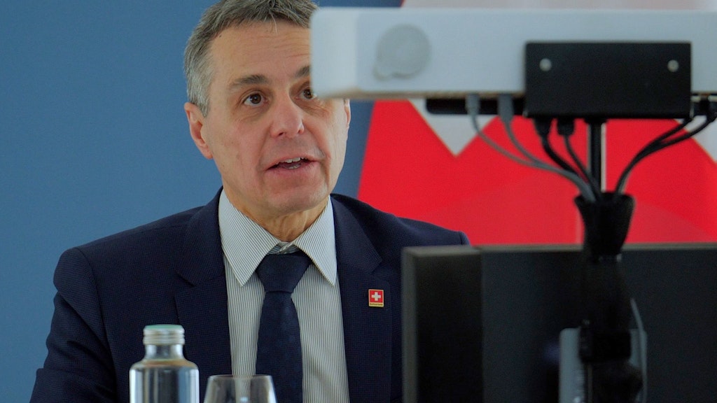 Le conseiller fédéral Ignazio Cassis prononce un discours face à une caméra lors d’une conférence virtuelle. Derrière lui, le drapeau de la Suisse.