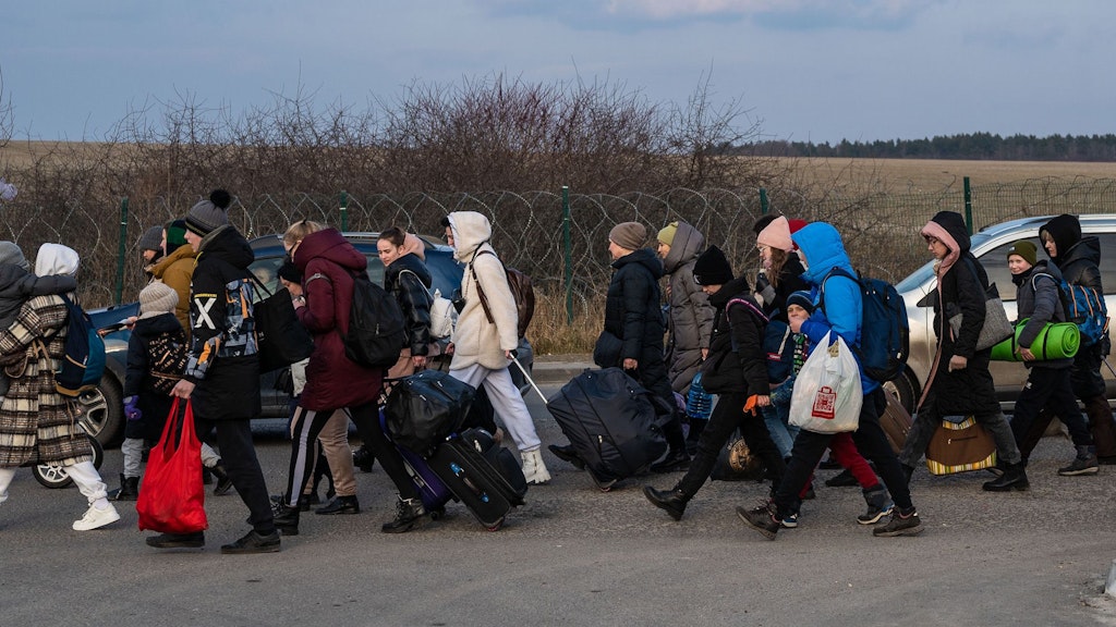 La photo montre un groupe de réfugiés voyageant avec des bagages. Ils sont habillés chaudement et se déplacent à pied dans une région rurale.