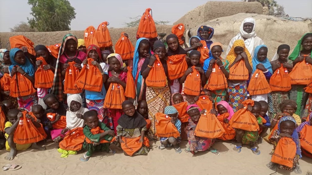 Children hold an orange school bag distributed by the NGO Norwegian Refugee Council.