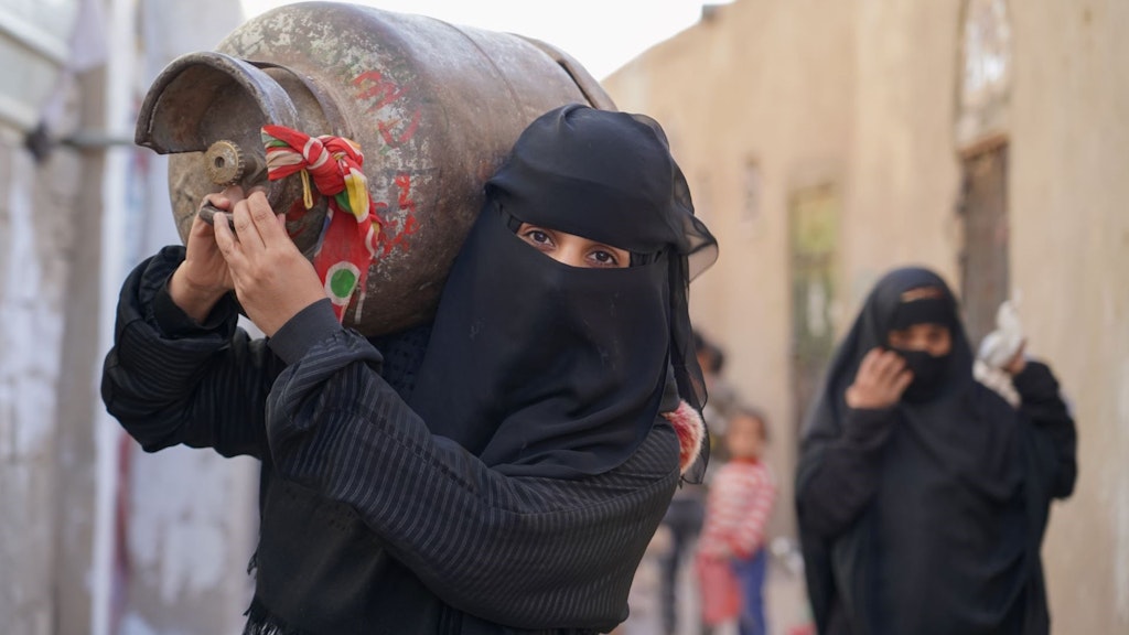 Une femme porte une bouteille de gaz pour les besoins de son foyer.