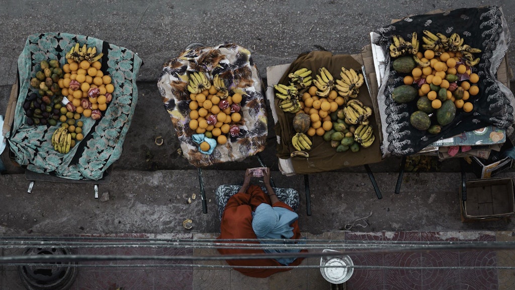 Vue aérienne d’une marchande de fruits au camp de réfugiés de Kakuma, au Kenya, assise devant un étal coloré.