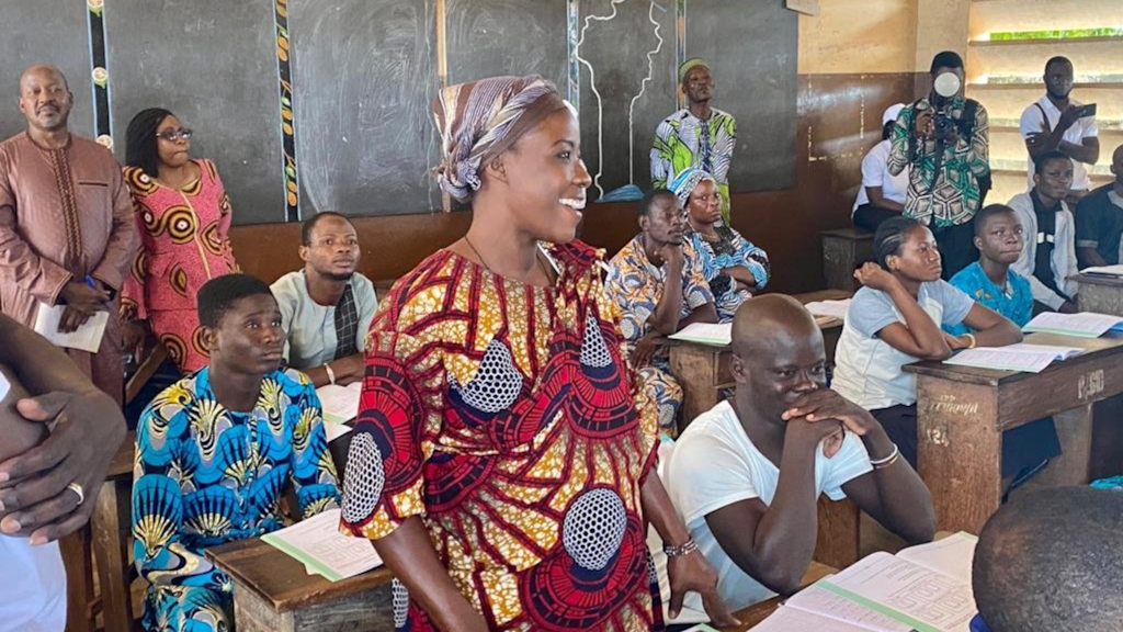 Une femme adulte se tient dans une salle de classe et s'adresse aux participants.