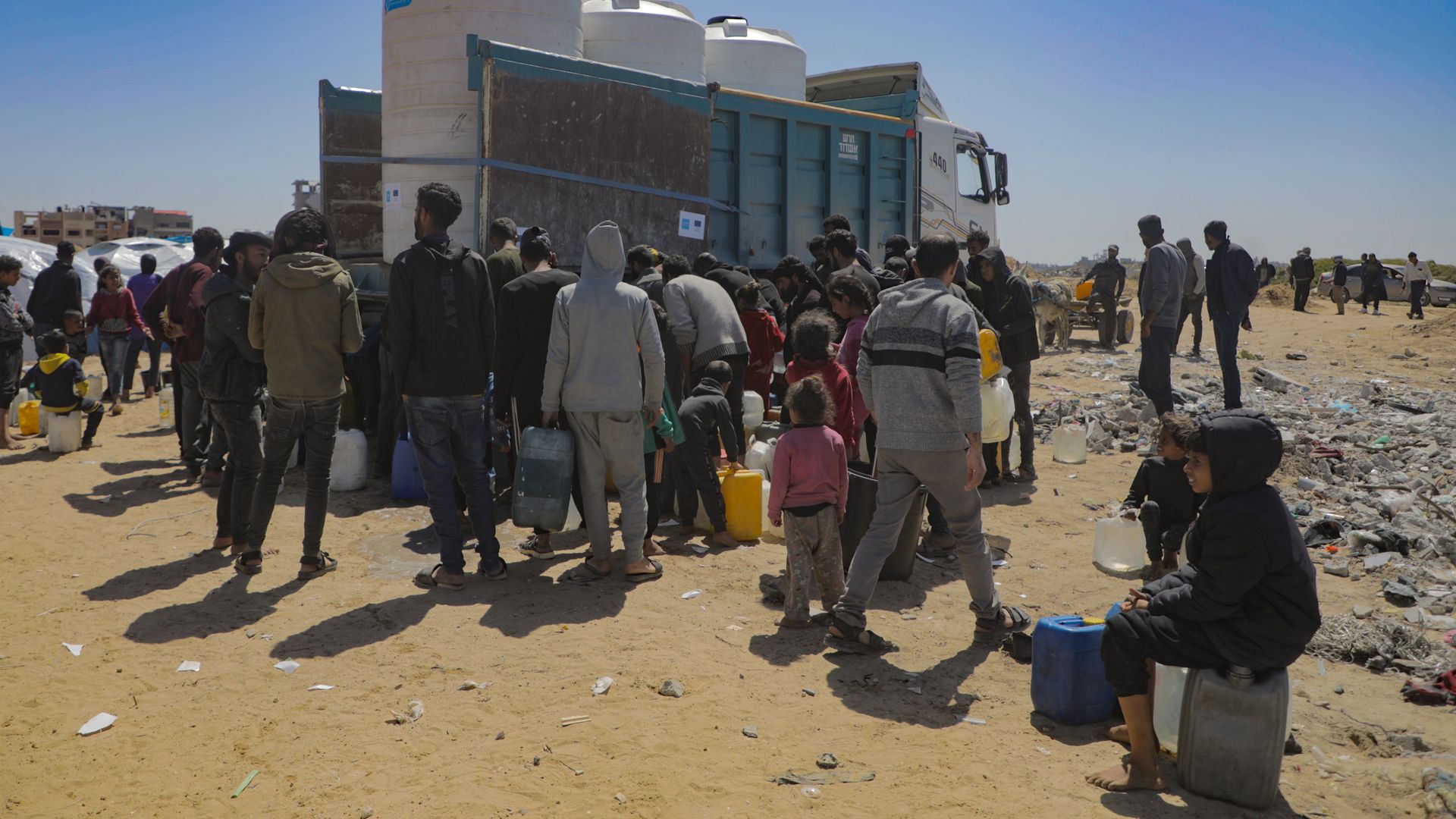 People with water containers are standing around a truck loaded with water tanks.