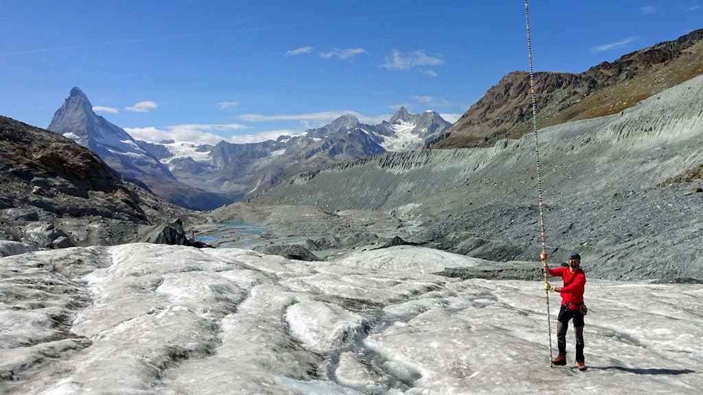 Un homme équipé d’une perche de mesure sur un glacier dans les Alpes suisses.
