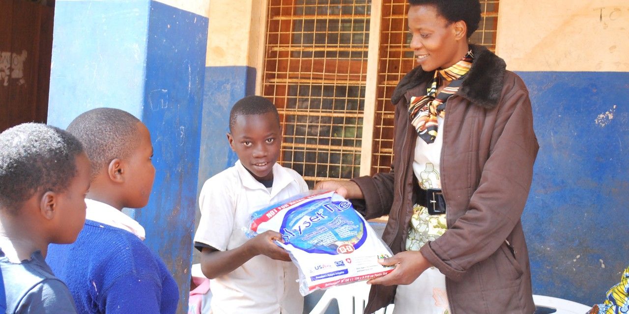 Eine Frau übergibt einem Kind ein Moskitonetz. Zwei weitere Kinder warten in der Schlange. 