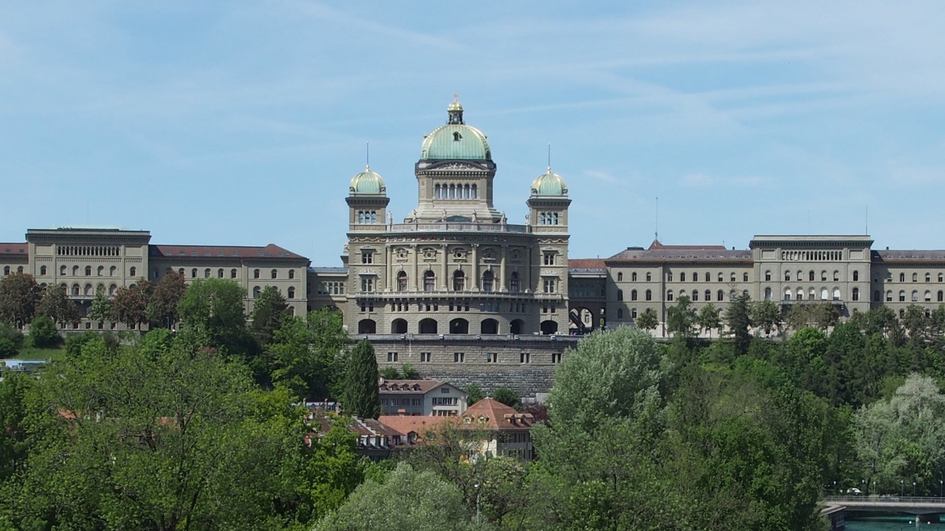 Das Bundeshaus in Bern mit grüner Kuppel, umgeben von Bäumen.