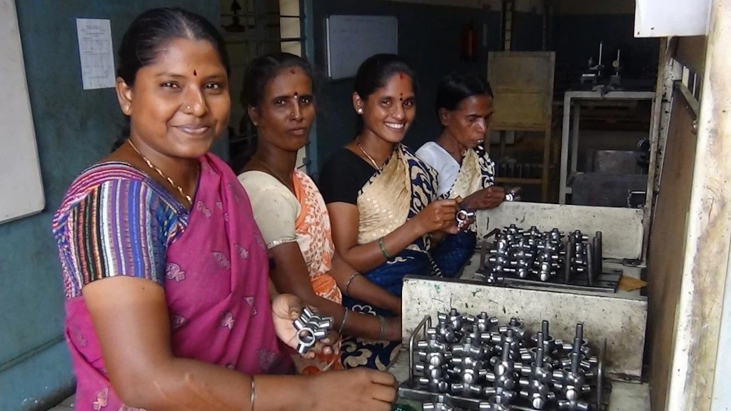 Auf dem Bild posieren vier Frauen indischer Herkunft lächelnd vor den zu montierenden Metallteilen.