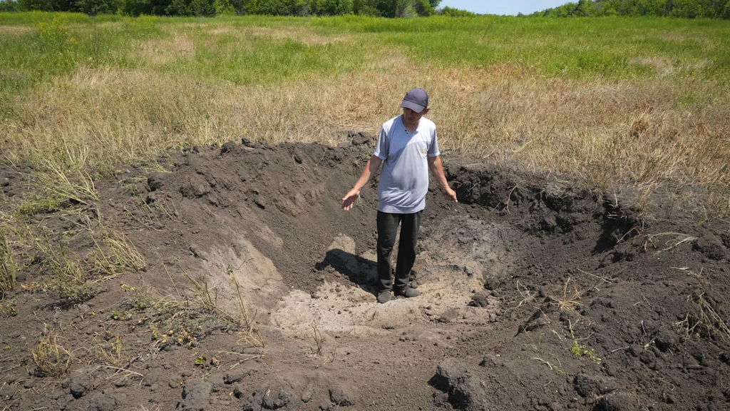 Ein ukrainischer Landwirt zeigt den Krater, den eine russische Granate in seinem Feld hinterlassen hat.