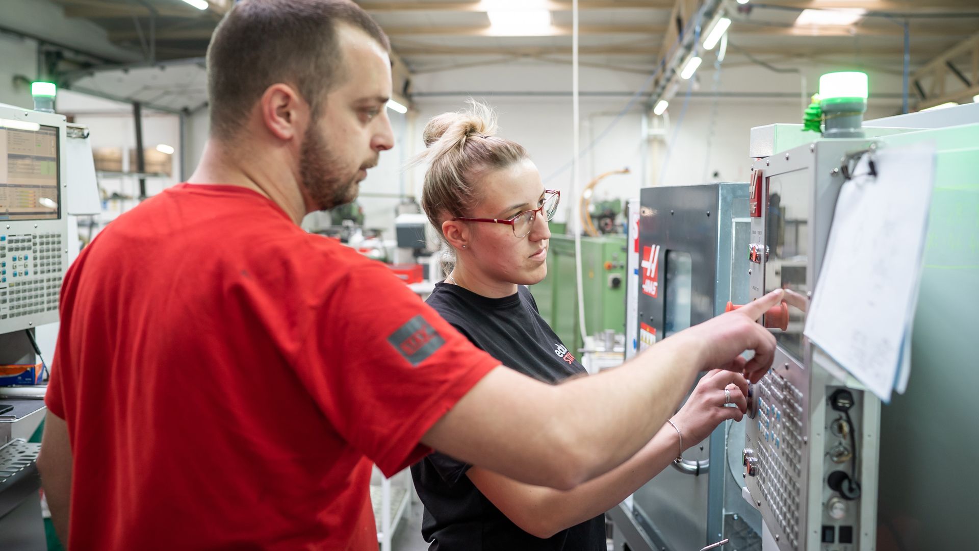 Ein Ausbilder erläutert einer Kursteilnehmerin die Bedienung einer Maschine.