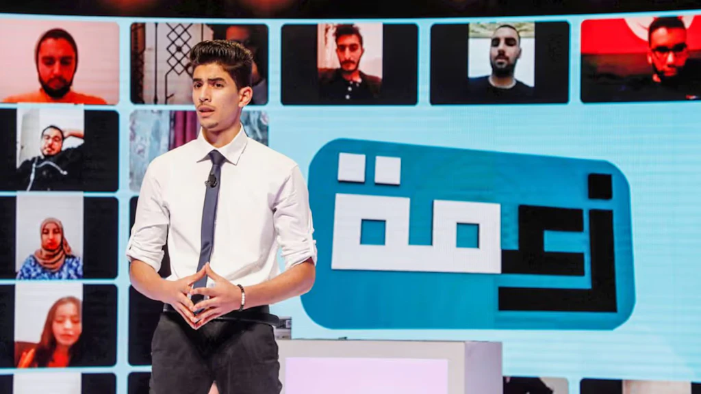 A young journalist stands in front of a giant screen and presents the news.