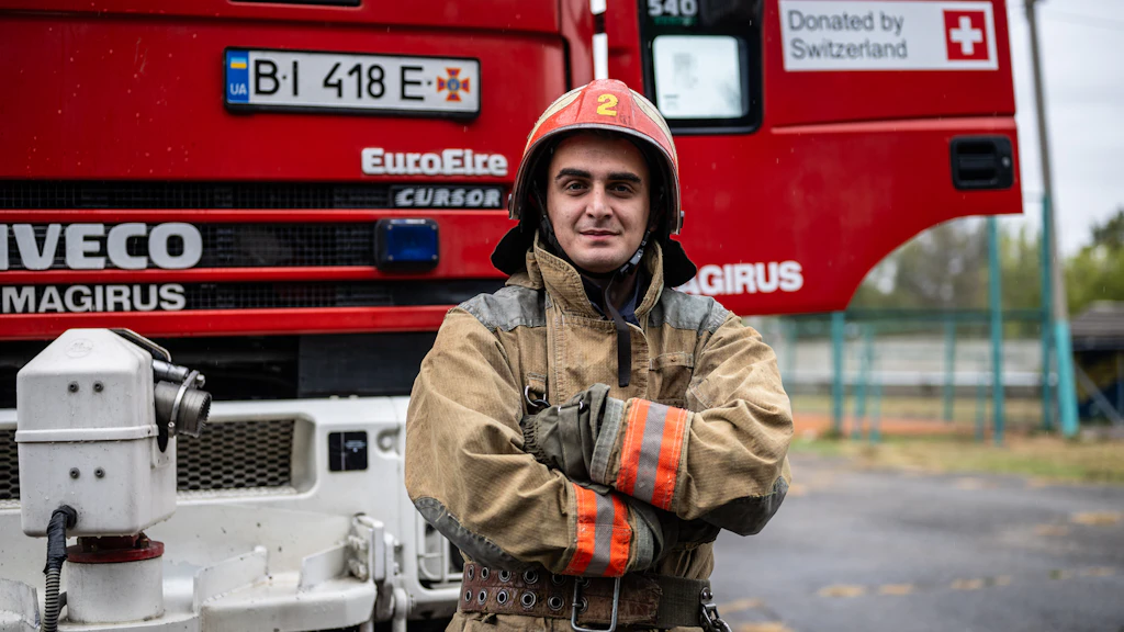 A Ukrainian firefighter stands in front of a fire engine donated by Switzerland, illustrating Swiss support to emergency response services in Ukraine.