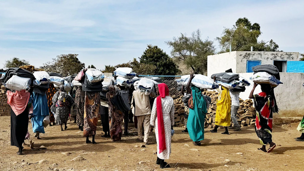 Displaced men and women walk with their backs to the camera, carrying on their heads bags of essential items distributed by the DRC. 