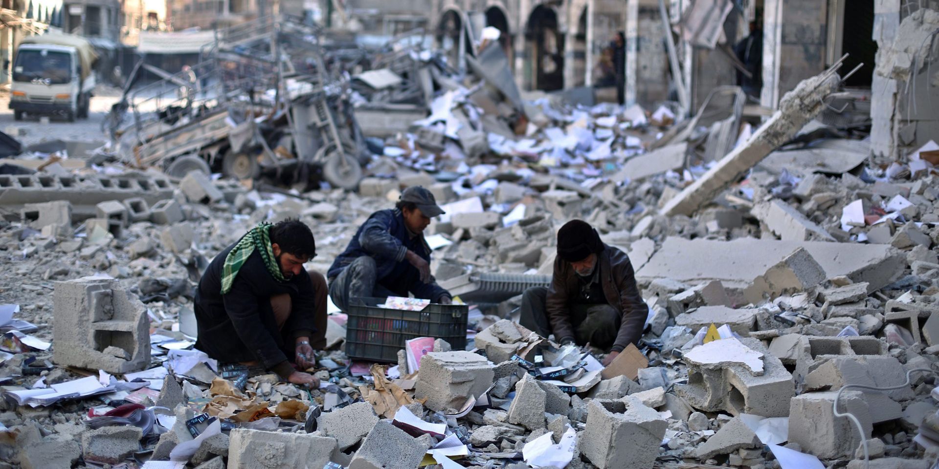 Three men, surrounded by a sea of rubble, pick through the debris of a building destroyed in an air strike.