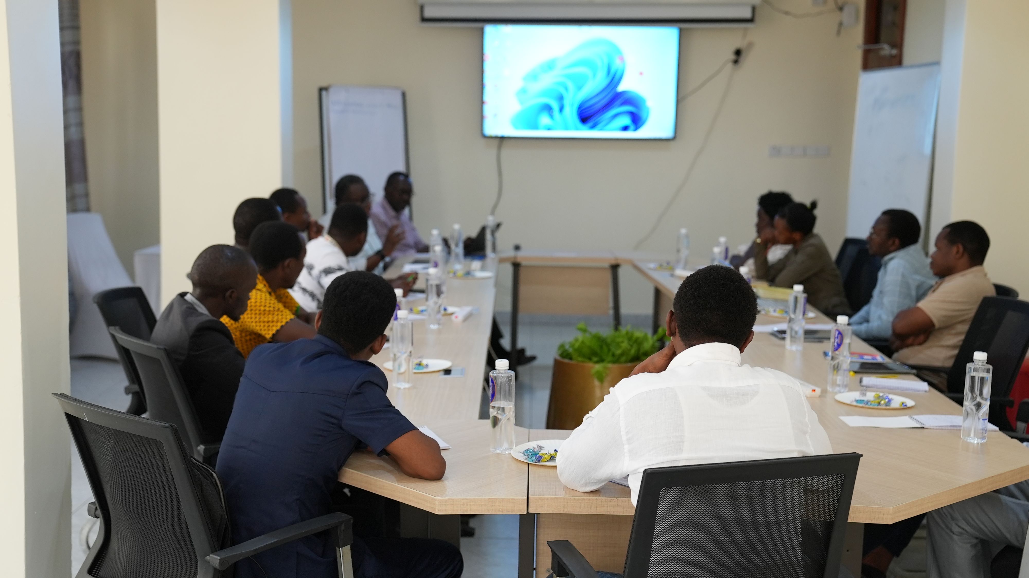 A group of 14 people are sitting around the table. They each have a bottle of water and cardboard plate. Someone on the left-hand side of the table is speaking.