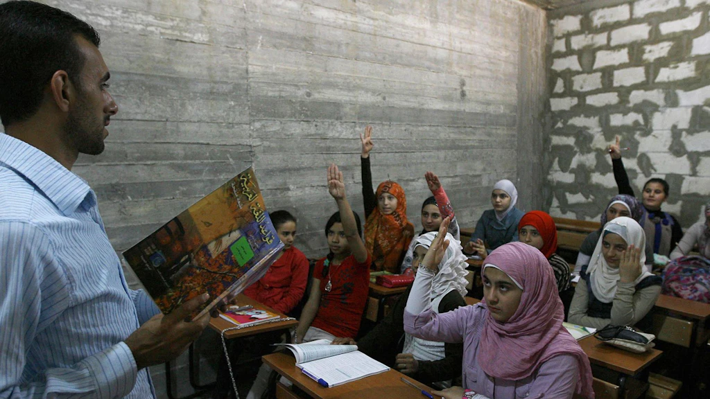 Syrian refugee girls sit in a classroom in Lebanon and stretch their hands.