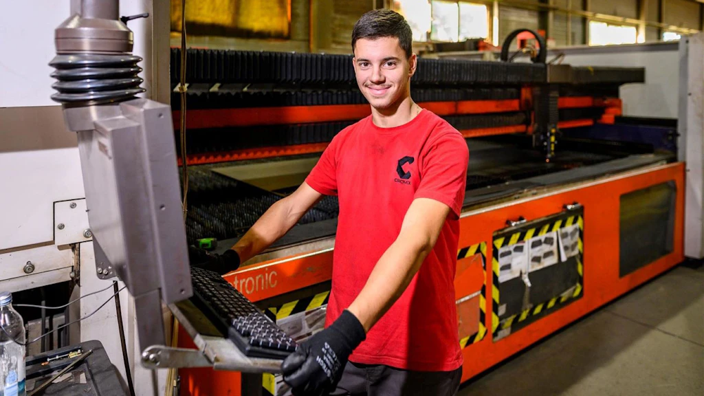 A young employee operating a production machine in an industrial plant.