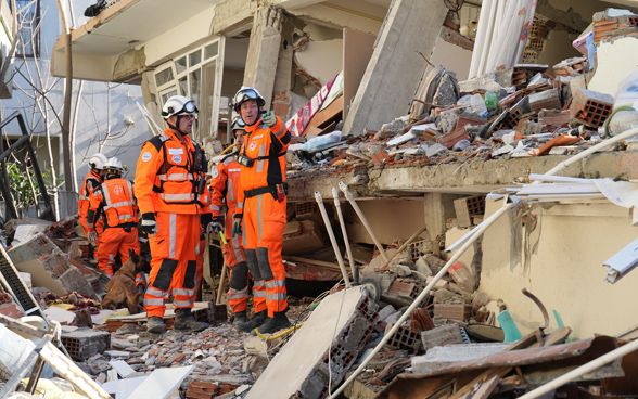 Two members of the rescue chain stand in front of a building whose outer wall has collapsed.