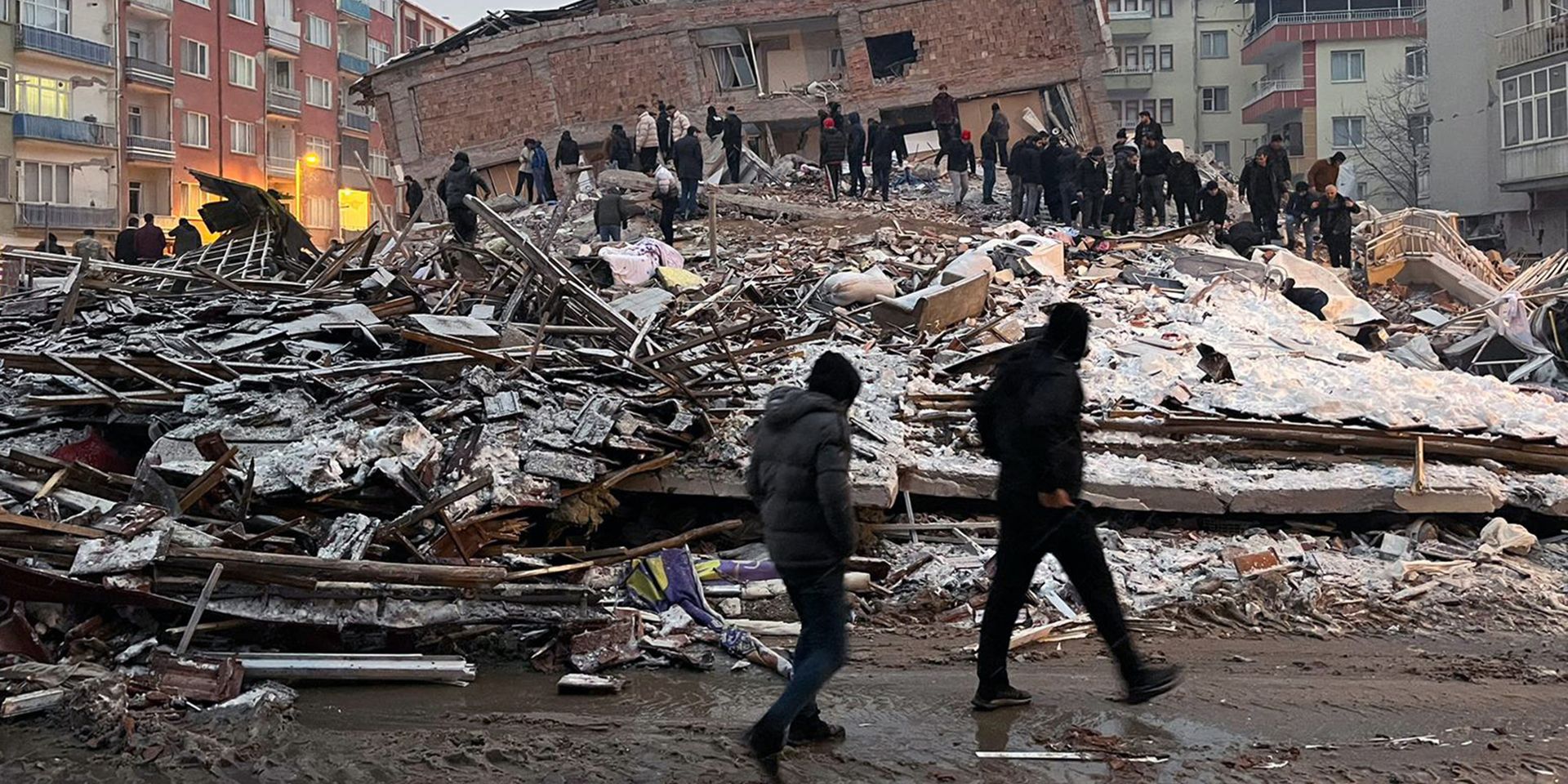 Several people standing in the rubble of a collapsed house. 