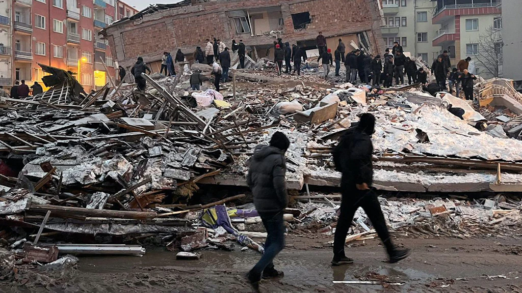 Several people standing in the rubble of a collapsed house. 