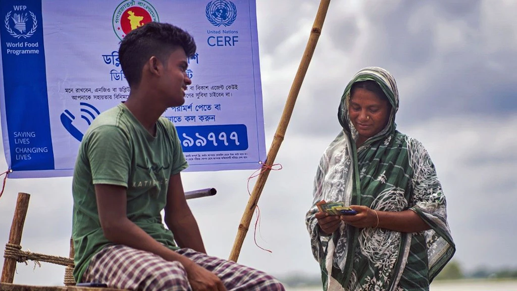 At the bank of a river in Bangladesh, a woman, with her son at her side, counts the cash assistance she received through an anticipatory action programme.