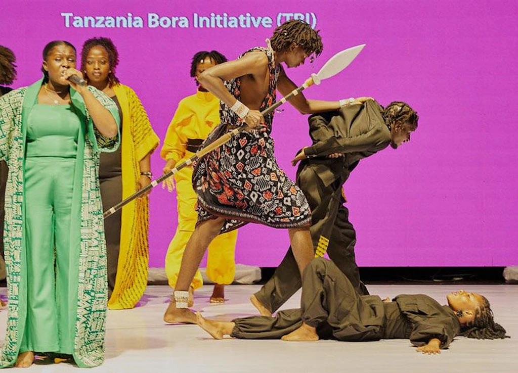 Performers on stage enacting a Massai warrior arresting a perpetrator.
