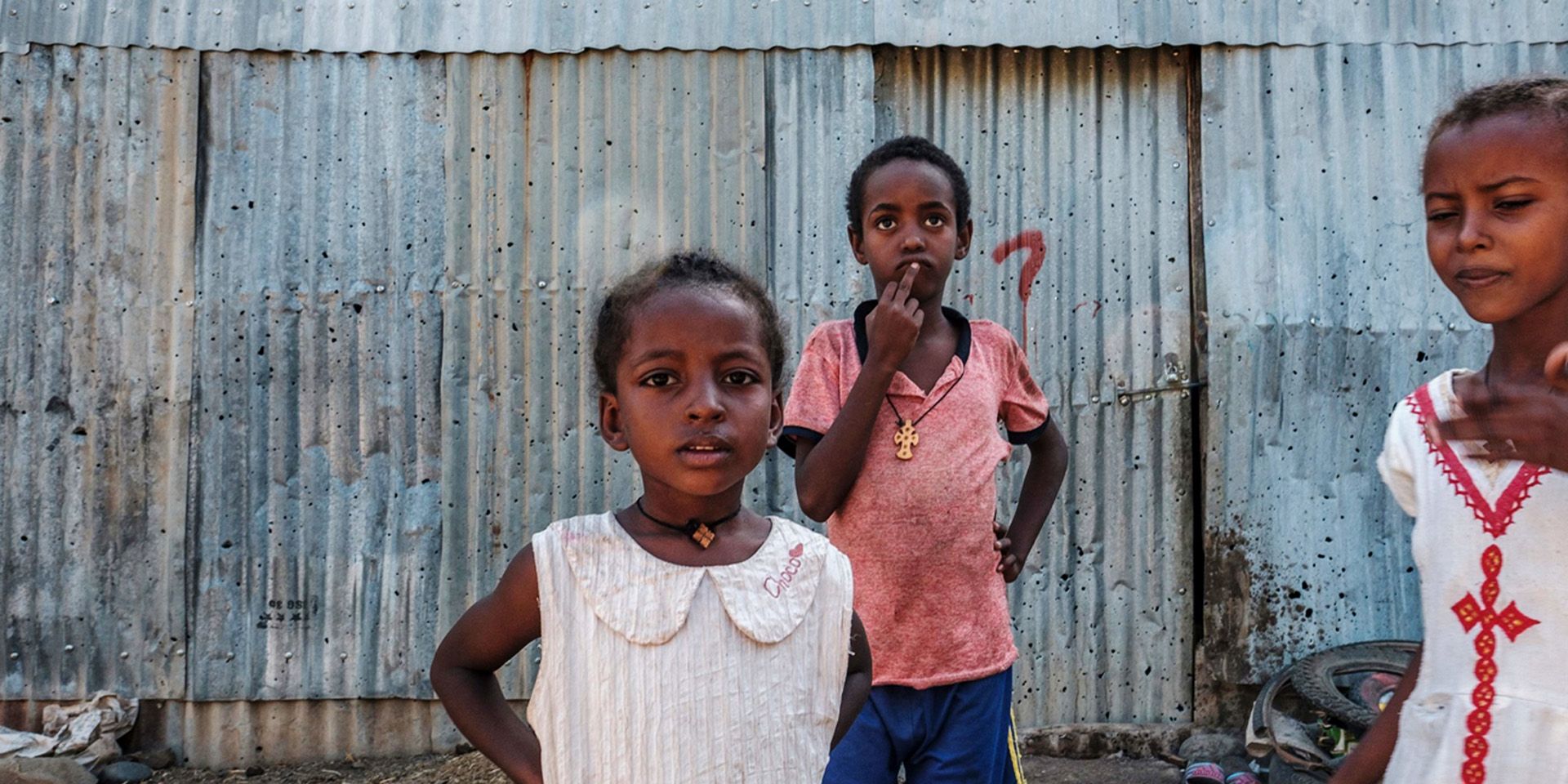 Young girls stand in front of a sheet-metal house in Humera, Ethiopia.