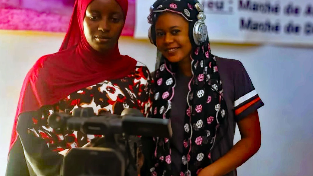 Two women, one by a camera, the other wearing headphones, on the set of a film. 