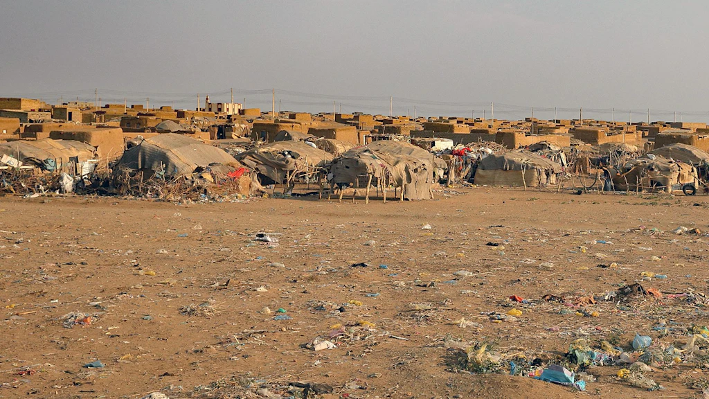 Tents and earthen shelters belonging to internally displaced people stand on the horizon. 