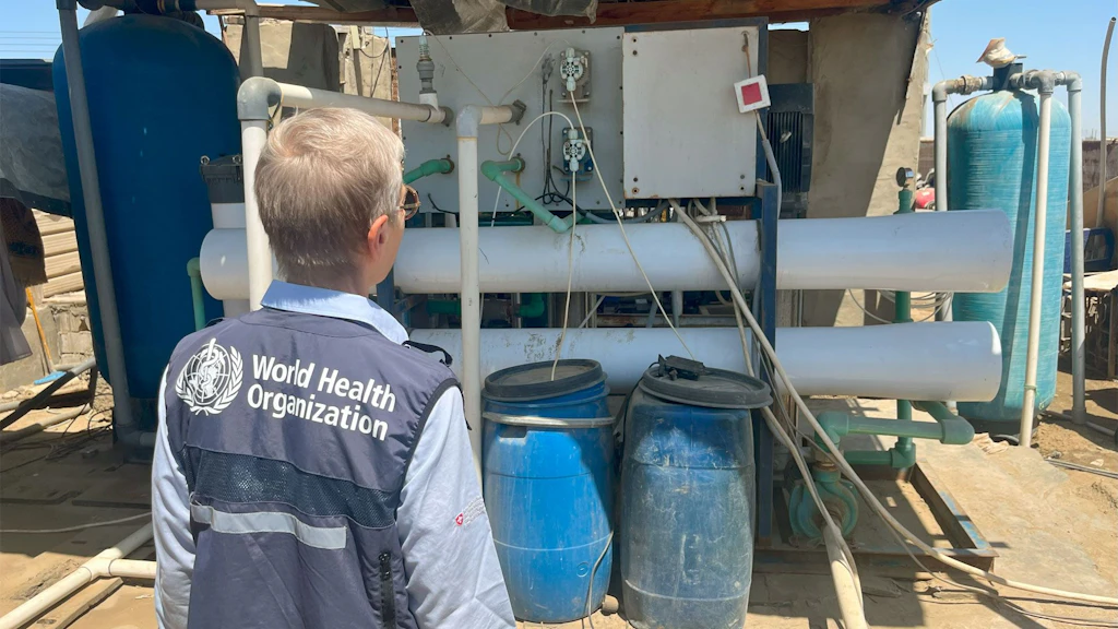 A woman in a blue vest with the WHO badge looking at the water-treatment equipment at a small private company in Port Sudan.