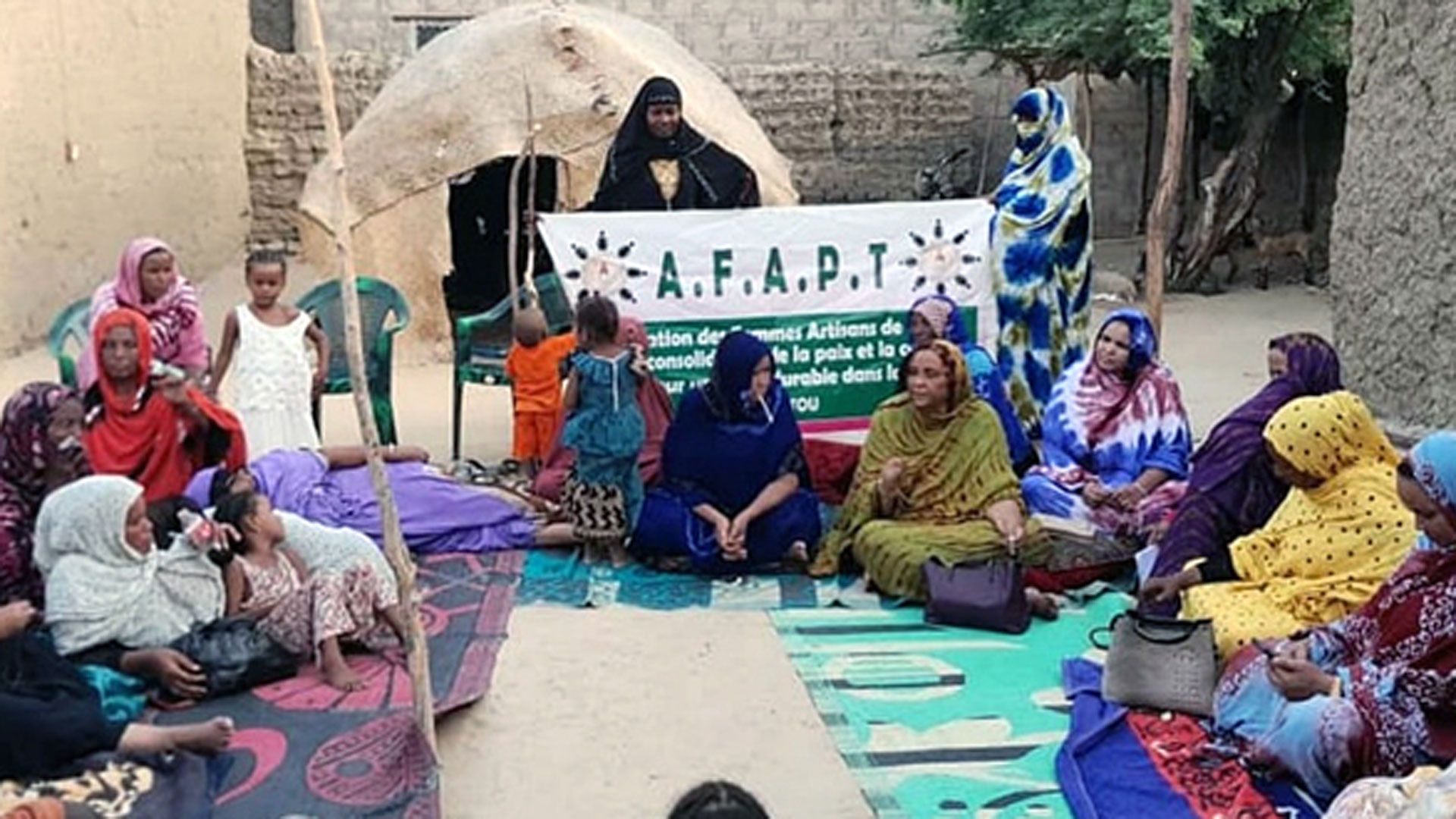 A group of women is sitting on the floor in a circle, legs crossed, and discussing among each other