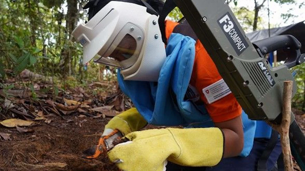 A woman wearing a helmet and protective vest defuses an explosive device.