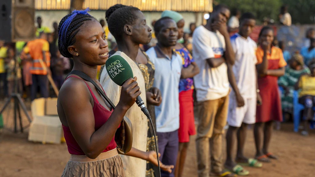 A young woman speaking into a green microphone. The name of the broadcaster – Radio Ndeke Luka – is on the microphone in white lettering.