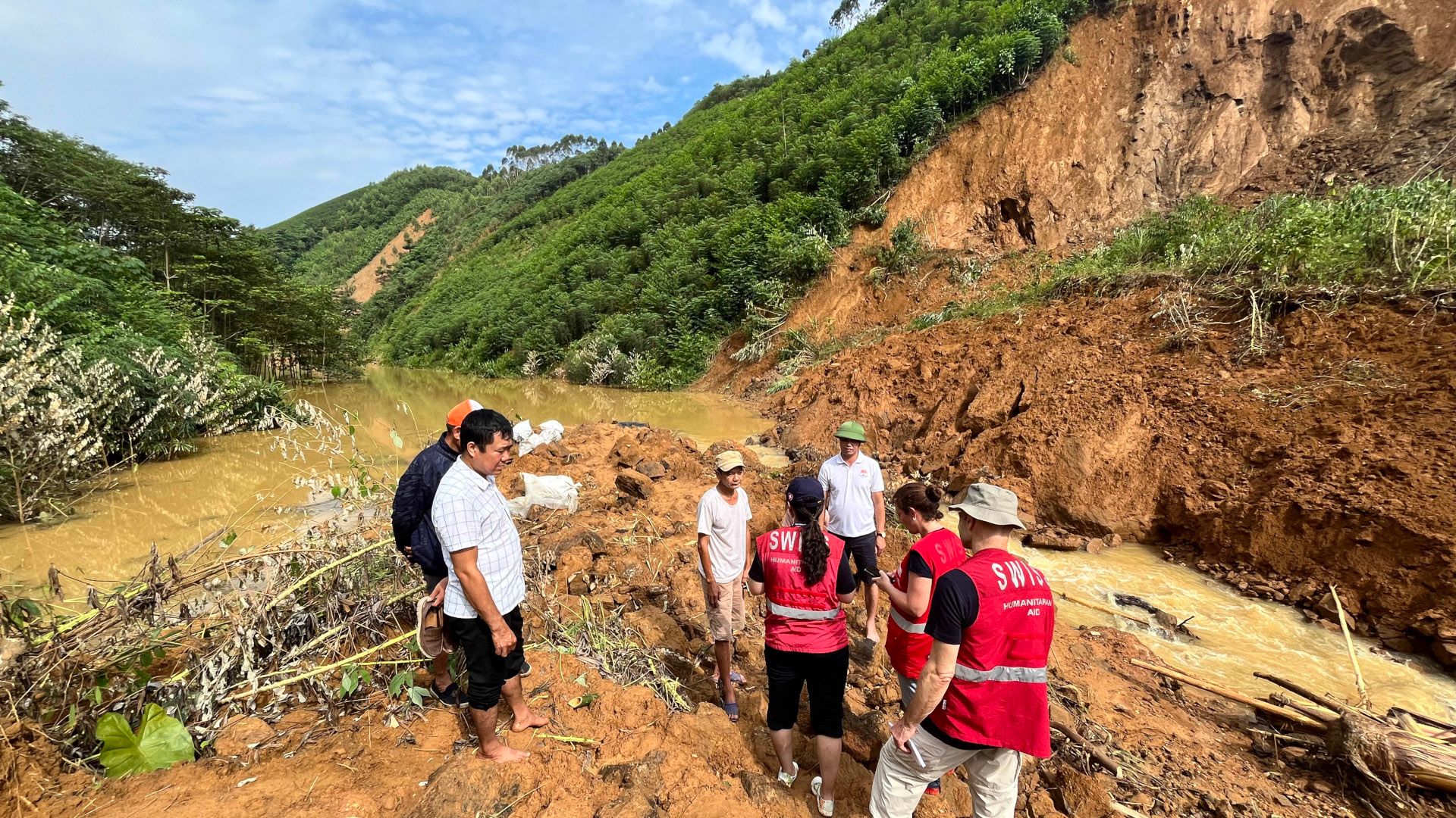 Three members of the Swiss Humanitarian Aid Unit speak with local people in an area affected by a landslide.
