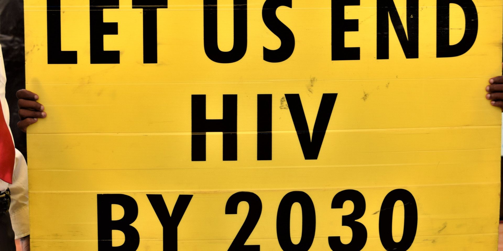 A young man holds up a yellow poster that reads: «We want to defeat HIV by 2030.»