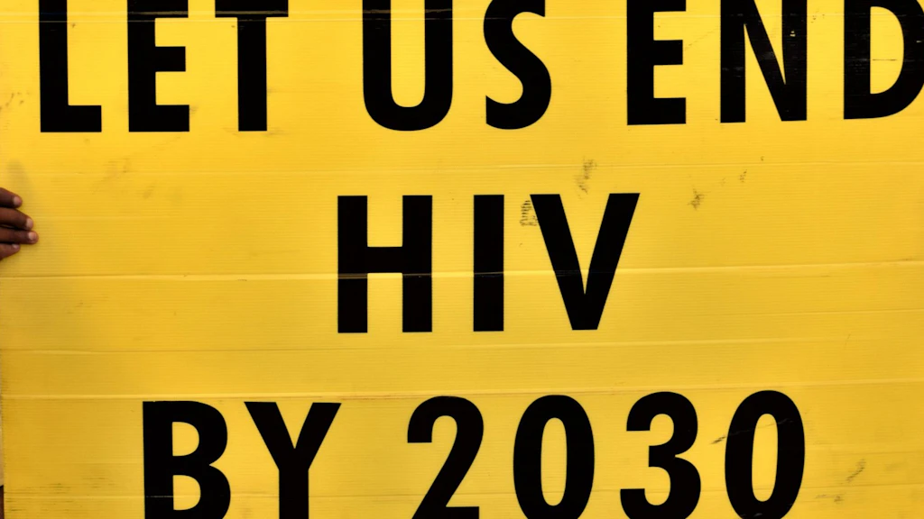 A young man holds up a yellow poster that reads: «We want to defeat HIV by 2030.»