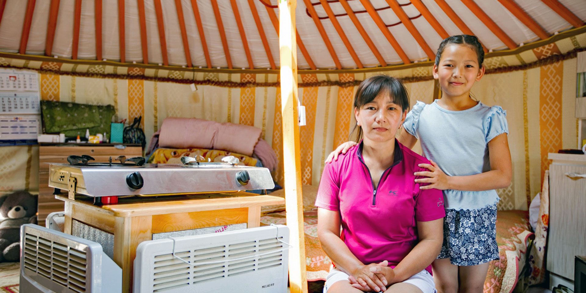 Mother and daughter next to a new, modern CHIP heating system in their traditional yurt.