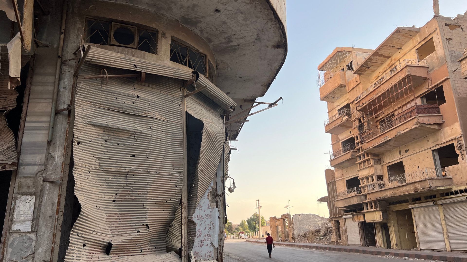 A man walks beside a war-damaged building.