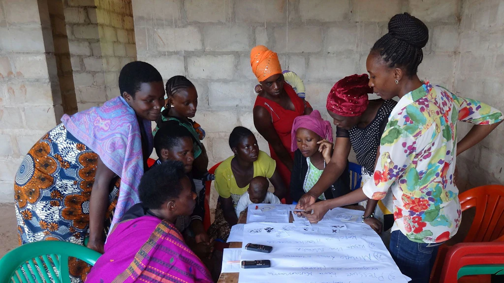 A group of women work at a table in Tanzania. Papers are laid out on it.