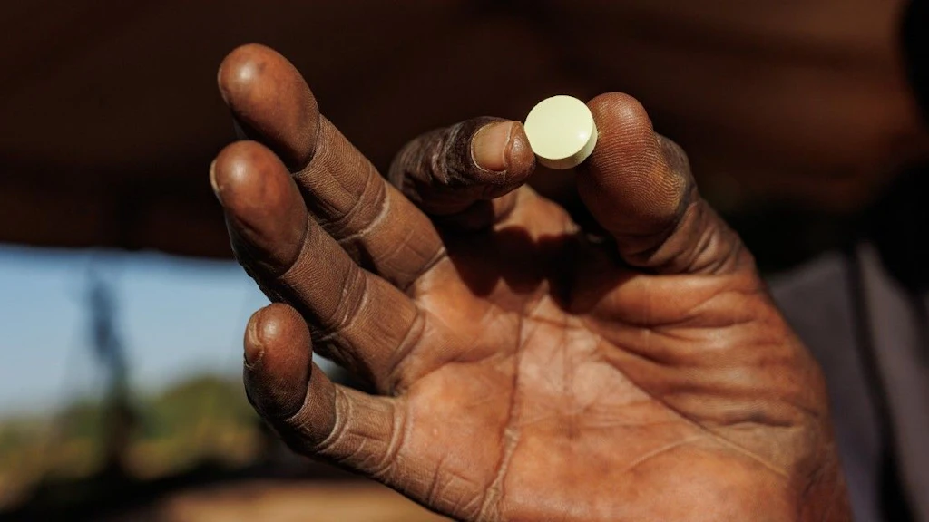 A hand holds a life-saving white pill between index finger and thumb.