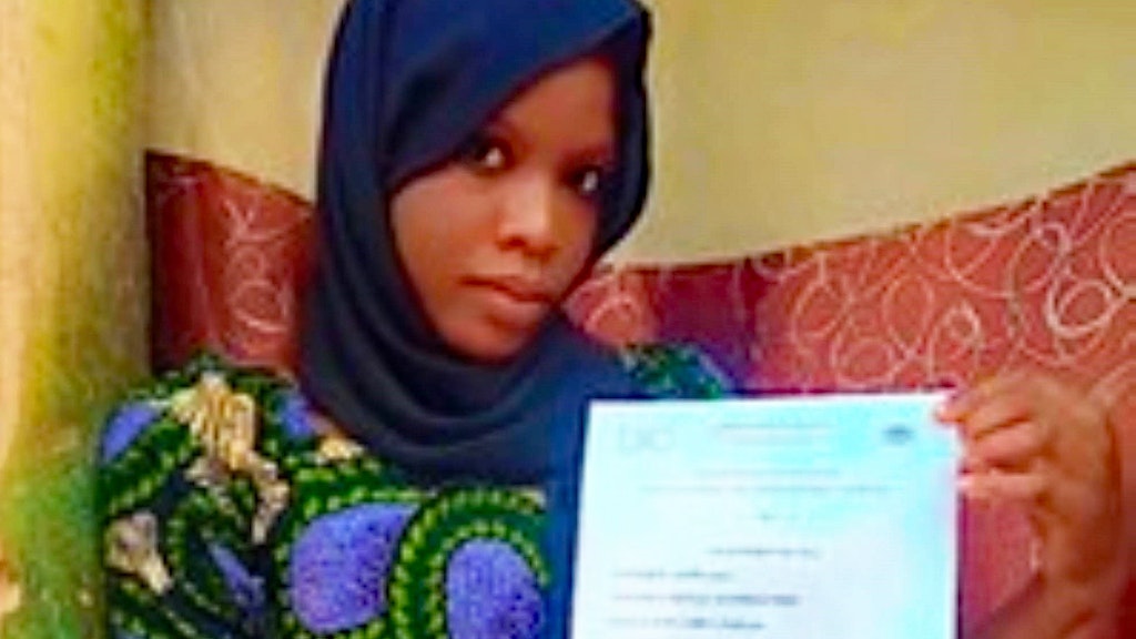 A young woman in a dress with colorful patterns and a blue headscarf holds her diploma in her hands.