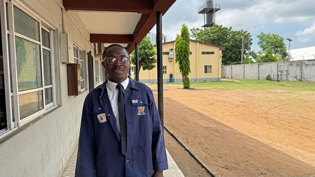 Ayinde stands in front of a building at the Lagos Technical College.