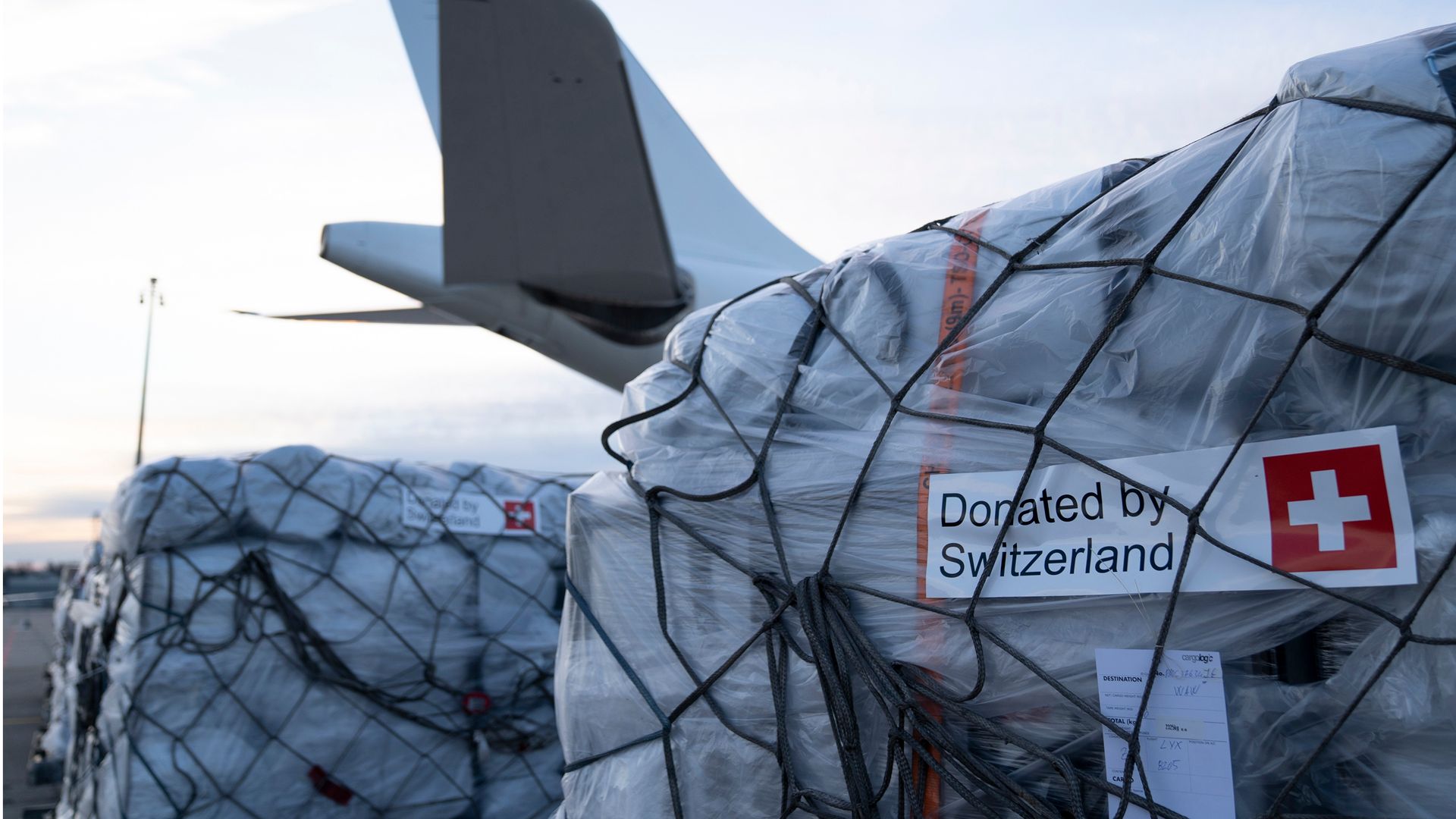 A pallet of humanitarian aid boxes in front of an airplane.