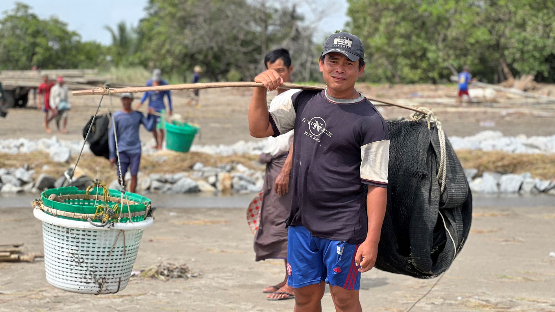 A worker in the wetlands of the Gulf of Mottama carries a load on his shoulder and looks into the camera.