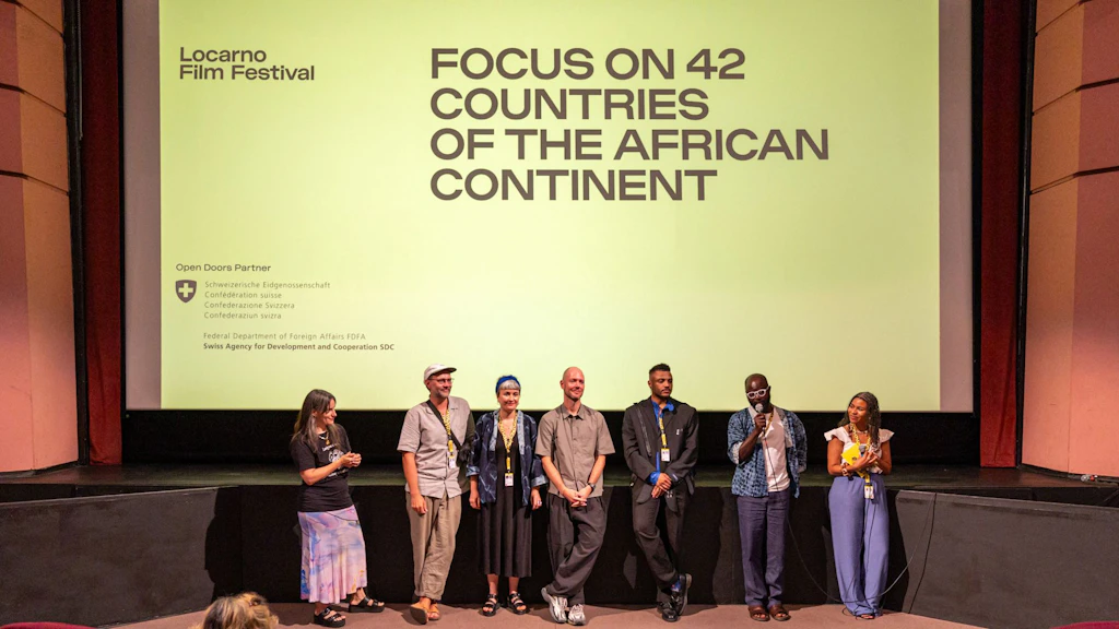 A group of people are gathered on a stage in front of a large cinema screen. They are answering questions using a microphone. 