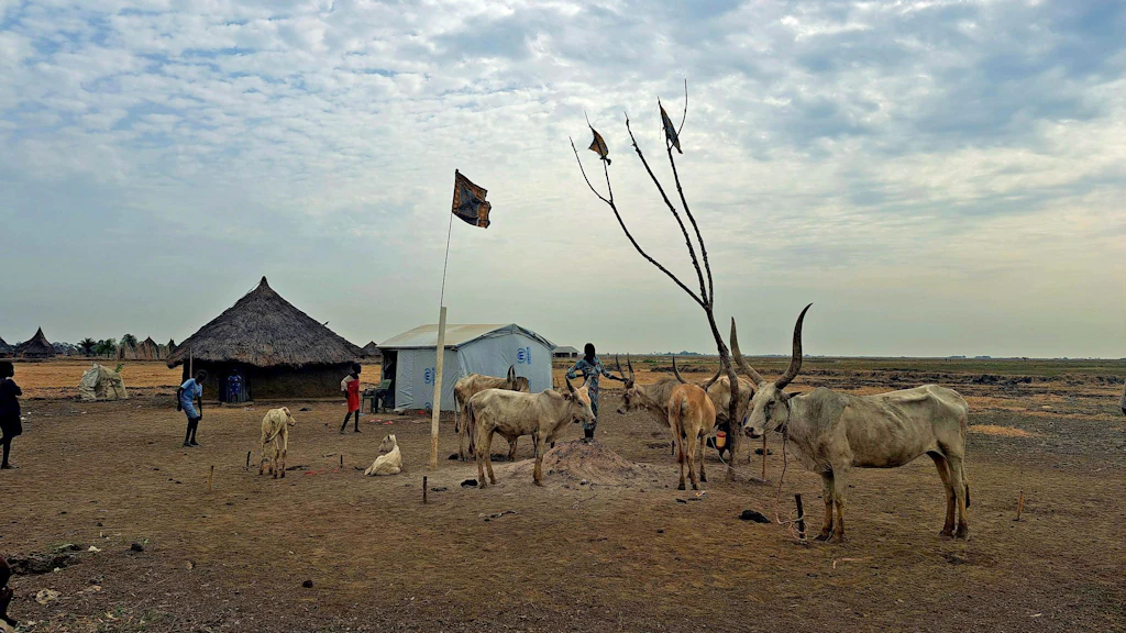 A landscape featuring some animals, a hut, and two men.